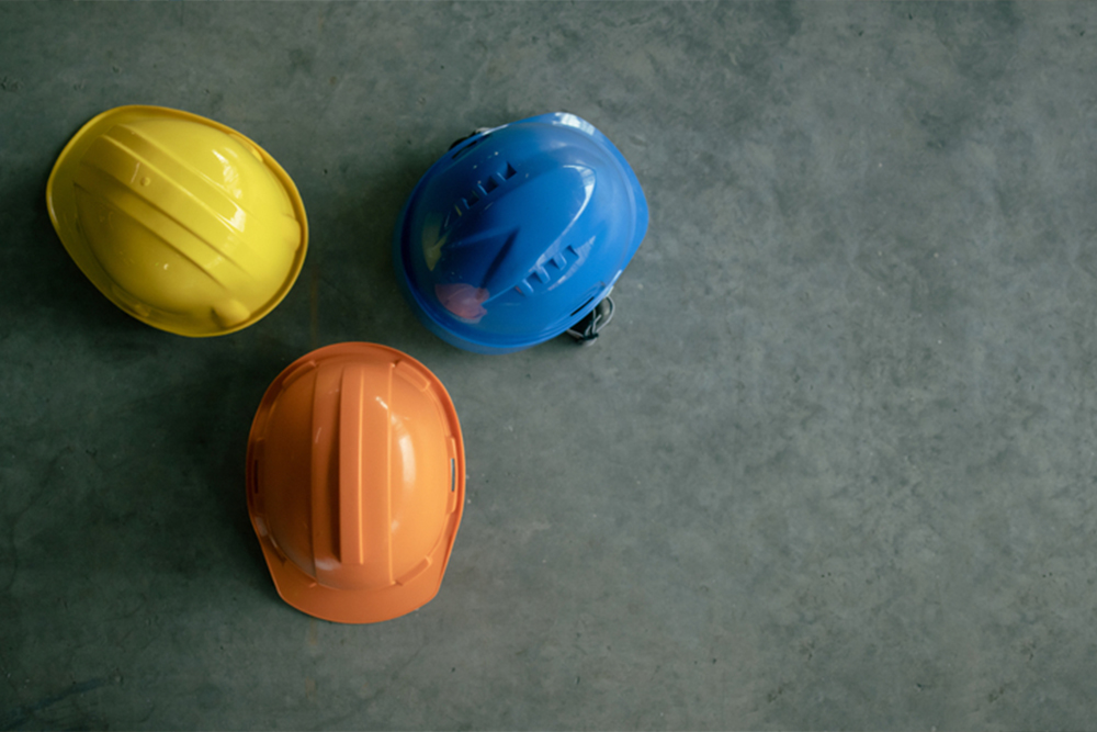 Three hard hats arranged on a concrete floor, showcasing their vibrant colors and sturdy design in a construction setting.