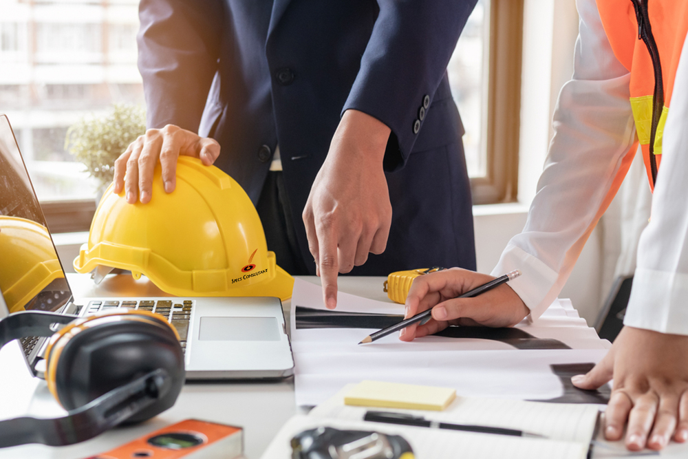 A man and woman in hard hats collaborate on a laptop at a construction site, focused on their work.