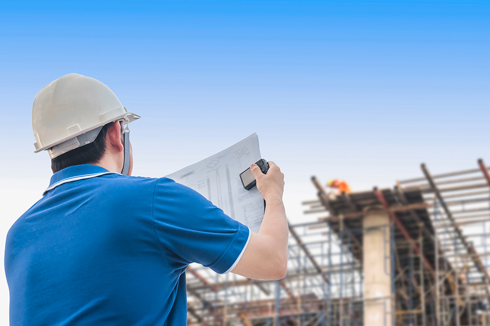 A man wearing a hard hat is holding a blueprint, focused on his construction project.