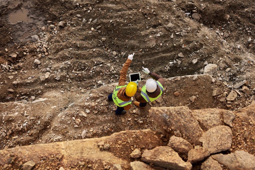 Two construction workers standing on a rocky hillside, wearing safety gear and surveying the construction site. Settlement joint and expansion joint فاصل الهبوط وفاصل التمدد